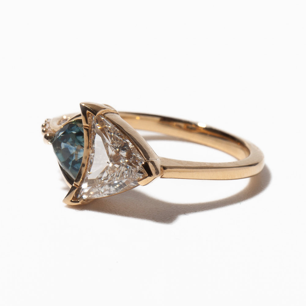 Close-up of trillion cut lab grown diamond engagement ring featuring teal sapphire side stones and unique geometric styling
